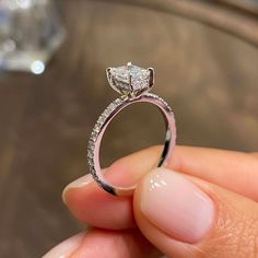 a close up of a person holding a ring with a princess cut diamond on it