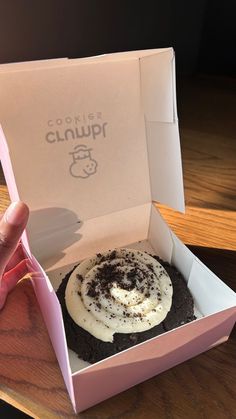 a person is holding up a box with a cupcake in it