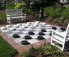 a checkerboard chess board in the middle of a garden with two white chairs