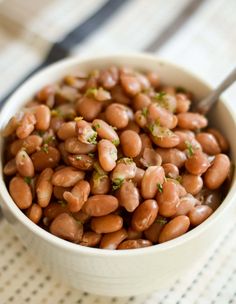 a white bowl filled with beans sitting on top of a table next to a fork