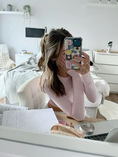 a woman taking a selfie with her phone in front of her face while sitting on a bed