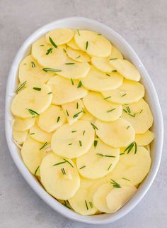 sliced potatoes in a white bowl with rosemary sprigs on top, ready to be cooked