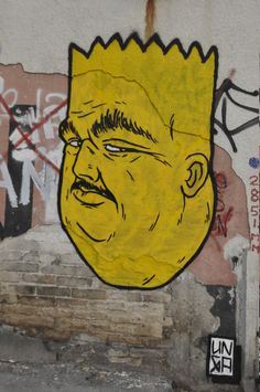 a yellow face painted on the side of a building with graffitti around it