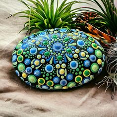 a painted rock sitting on top of a sandy beach next to plants and pineapples