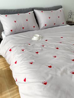 a bed with white sheets and red hearts on it, along with a cup of coffee