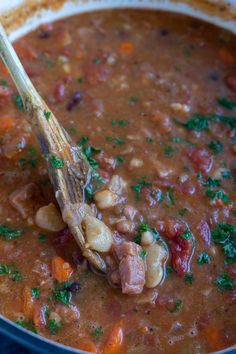 a wooden spoon in a pot filled with beans and ham soup, garnished with parsley