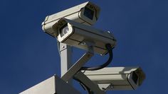 two security cameras on top of a brick building with blue sky in the back ground