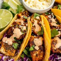 three fish tacos on a plate with cole slaw and lime wedges