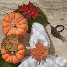 three pumpkins and two leaves sitting on top of a wooden table next to each other