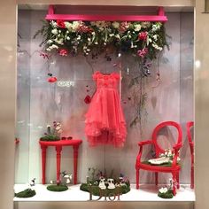 a display case filled with red chairs and pink dresses hanging on the wall next to each other