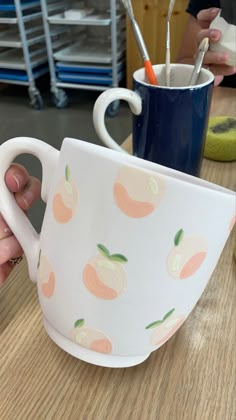 a hand holding a coffee cup with peaches painted on the outside and inside it