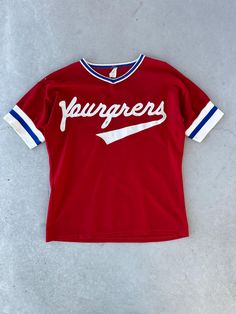 a red jersey with white lettering on the front and blue trim around the sleeves that says, fudgers