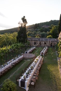 a long table set up in the middle of an outdoor setting with candles and place settings