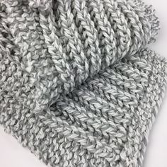 the grey and white knitted scarf is folded on top of another gray wool blanket