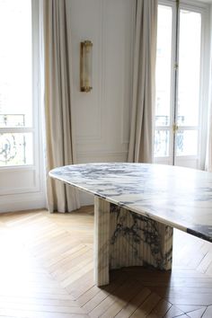 a large marble table sitting in front of a window next to a wooden parquet floor