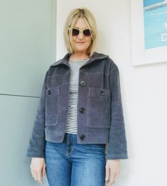 a woman standing next to a wall with her hands in her pockets