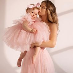 a woman in a pink dress holding a baby girl wearing a pink tutu skirt