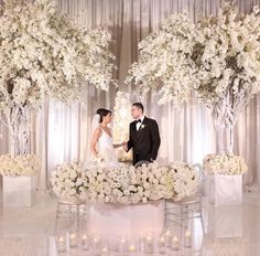 a bride and groom standing in front of a wedding cake with white flowers on it