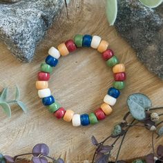 a bracelet made out of multicolored beads on a wooden table next to rocks and plants