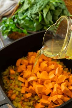 someone is pouring oil on some food in a pan with carrots and spinach