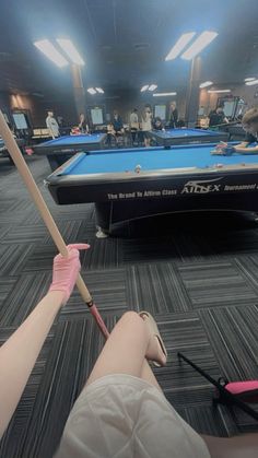 two people are playing pool in an empty room with other people watching from the sidelines