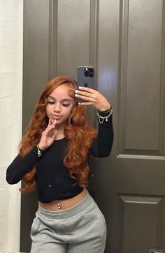 a woman with red hair taking a selfie in front of a mirror wearing grey sweatpants