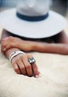 a woman laying in the sand with her hand on top of her wrist and wearing a white hat