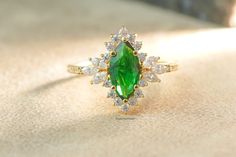 a ring with a green stone surrounded by white and yellow diamonds on a beige surface