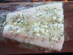 a piece of raw fish on a cutting board with herbs and seasoning sprinkles