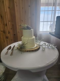 a white table with a cake and silverware on it next to a wooden wall