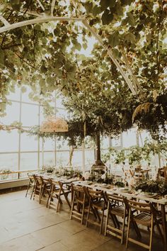 an indoor dining area with tables and chairs covered in greenery, surrounded by large windows