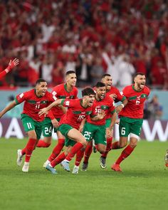 a group of soccer players running on the field during a game with fans in the background