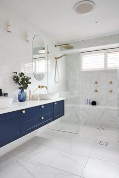 a white bathroom with blue cabinets and marble counter tops, along with a large walk in shower