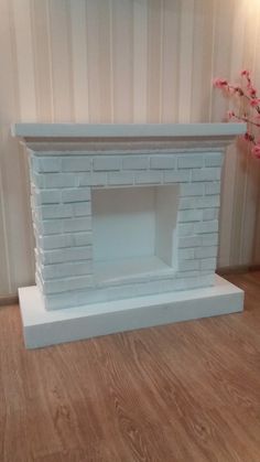 a white brick fireplace sitting on top of a hard wood floor next to a vase with pink flowers