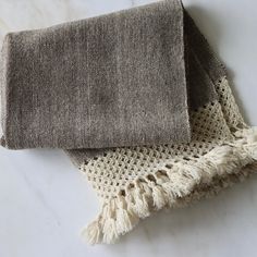 two pieces of woven fabric on a white counter top with some tassels around the edges