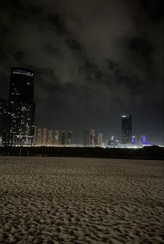 the city skyline is lit up at night with clouds in the sky and sand on the ground