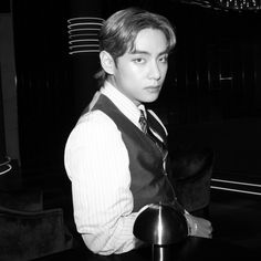 a young man in a vest and tie sitting at a table with a lamp on it