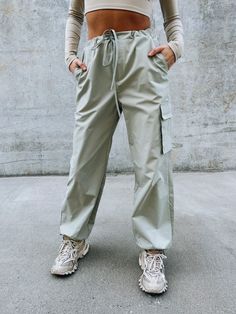 DETAILS: Our Logan Athletic Cargo Pant have an oversized fit with a soft nylon fabric. These cute bottoms have a ribbed stretchy band for a comfortable fit around the waist and there is also a self tie string to synch the waist. There are two side pockets, one flap pocket on the pant leg, and the bottom of the pants have a self tie string to synch it tighter around the ankle. Runs true to size but has an oversized look. CONTENT & CARE: SELF: 100% Polyester. SIZE & FIT: Model is 5'6" The model is Casual Bottoms With Cargo Pockets And Paperbag Waist, Sporty Khaki Cargo Pants For Spring, Sporty Khaki Parachute Pants For Spring, Sporty Spring Khaki Cargo Pants, Sporty Spring Cargo Pants With Functional Drawstring, Sporty Khaki Bottoms For Spring, Sporty Spring Cargo Pants With Drawstring, Spring Sporty Khaki Parachute Pants, Casual Spring Cargo Pants With Paperbag Waist