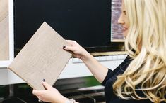 a woman is looking at some wood on the shelf in front of a computer screen