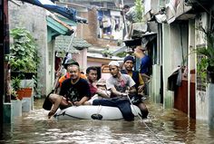 several people are riding on an inflatable boat through a flooded street with buildings