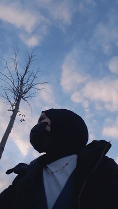 a person wearing a black mask standing next to a tree