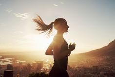 a woman running in the sun with her hair blowing in the wind over a city