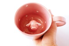 a hand holding a pink cup with a pig in it