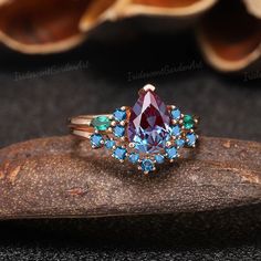 a ring with blue and green stones on it sitting on top of a piece of wood