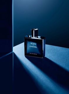 a bottle of chanel bleu de chanel on a blue surface with the light coming from behind it