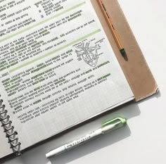 an open notebook with writing on it next to a green pen and a white background