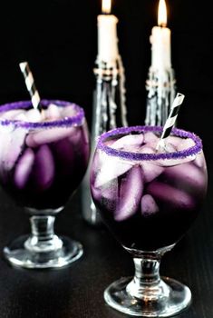 two glasses filled with purple liquid and lit candles