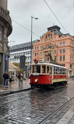 a red and white trolley car traveling down a city street next to tall buildings on a rainy day