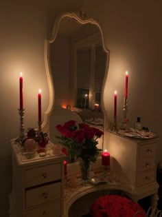 a dressing table with candles and flowers on it in front of a mirror that is lit up