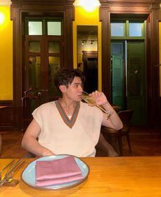 a man sitting at a table drinking out of a wine glass while holding a fork and knife